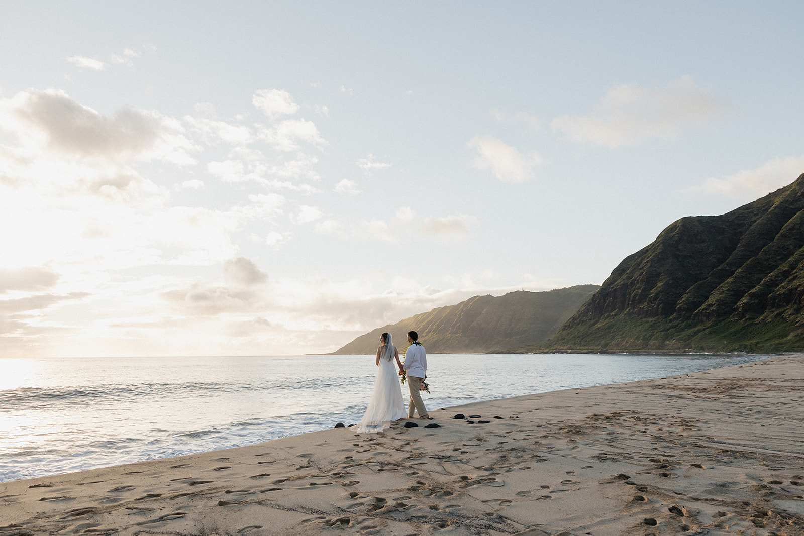 Bride and groom walking along the shoreline, mountains stretching out beside them.
