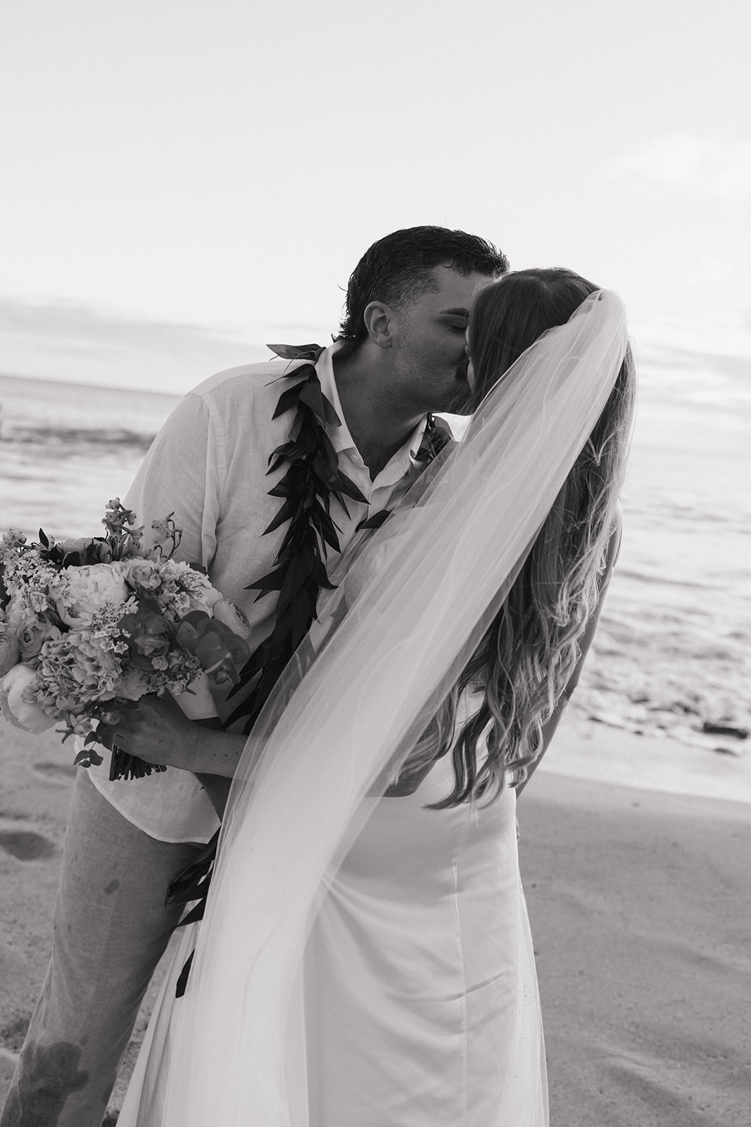 Black and white close-up of the couple kissing, her veil blowing across the frame.