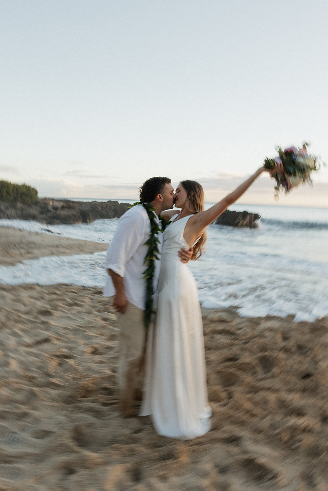 Motion shot of the bride and groom kissing while she throws her bouquet up in celebration.
