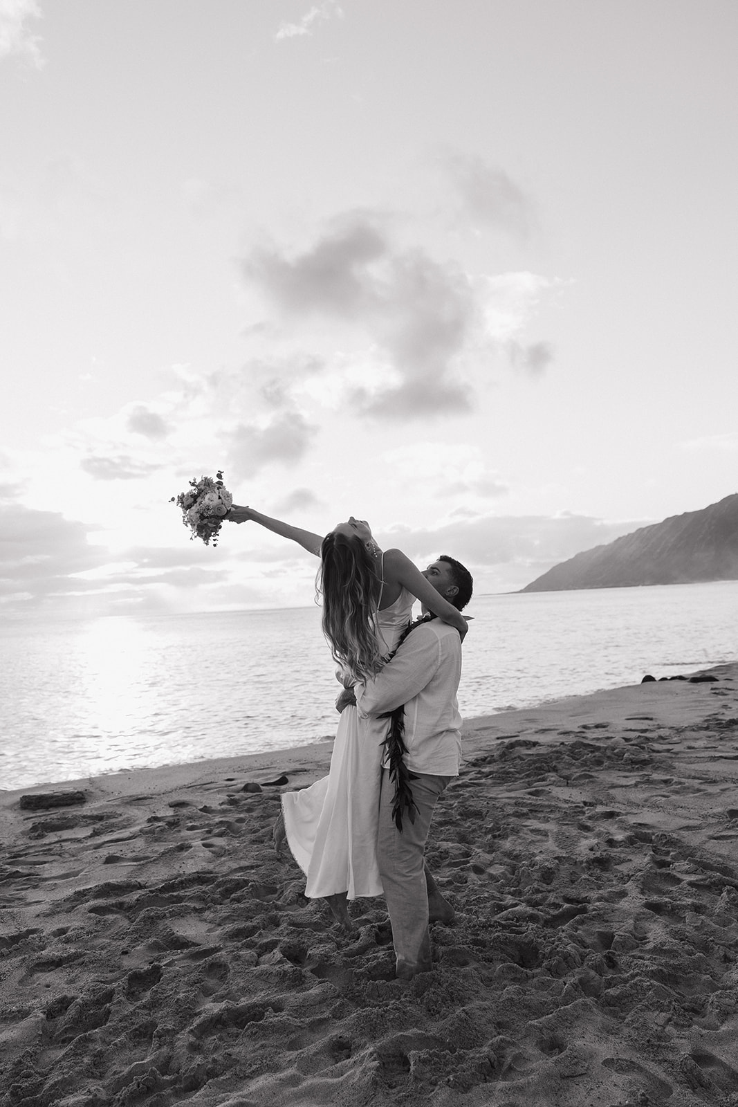 Black and white shot of the groom lifting his bride up as she raises her bouquet toward the sky.