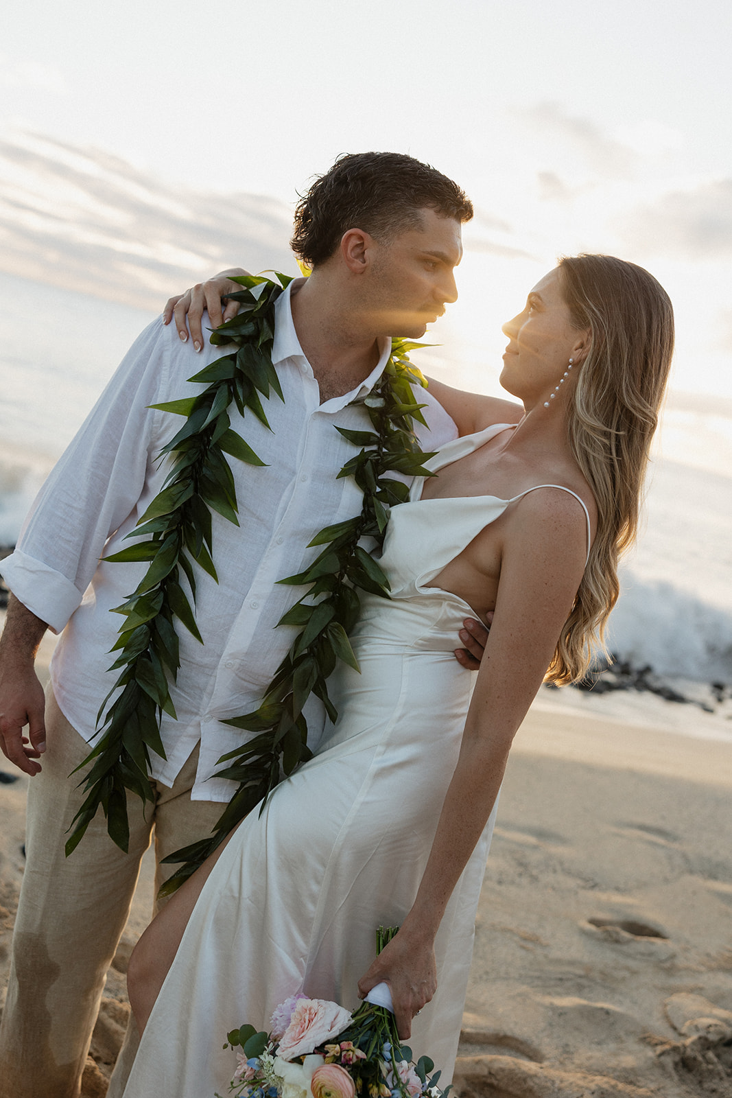 Bride and groom gazing at each other in the golden sunset light, her hand resting on his lei.
