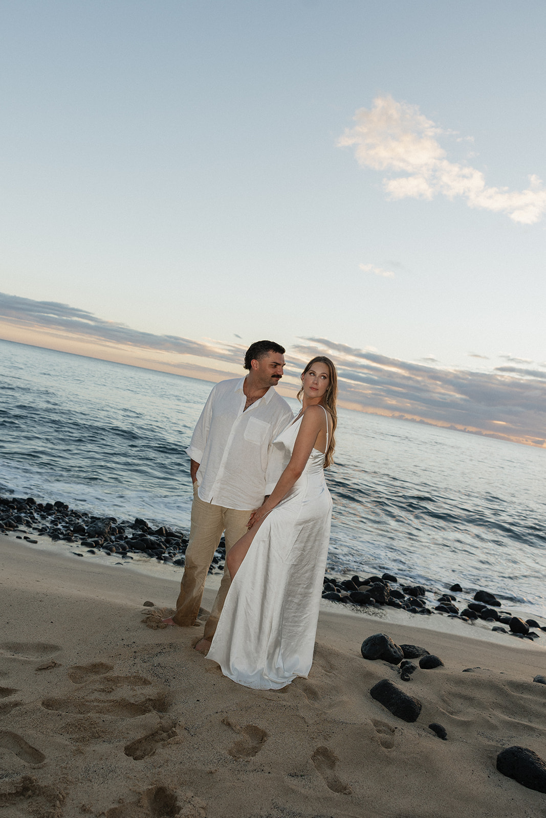 Bride and groom standing close together on a rocky shoreline during their beach elopement at sunset.