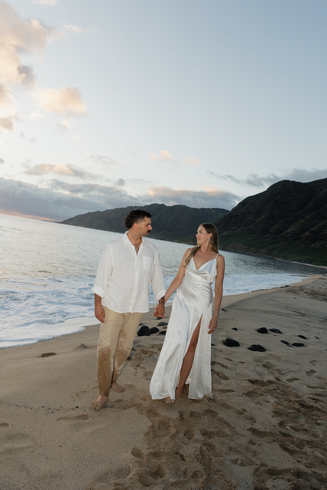 Groom looking back at his bride as they walk along the shoreline together.
