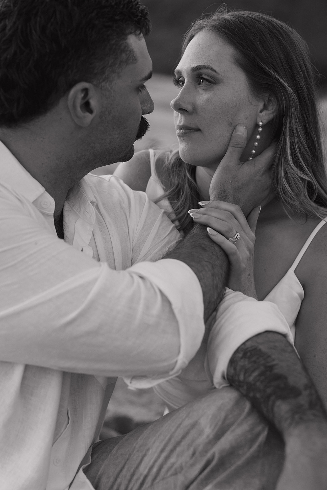 Close-up black and white shot of the groom holding his bride's face, her ring on full display.