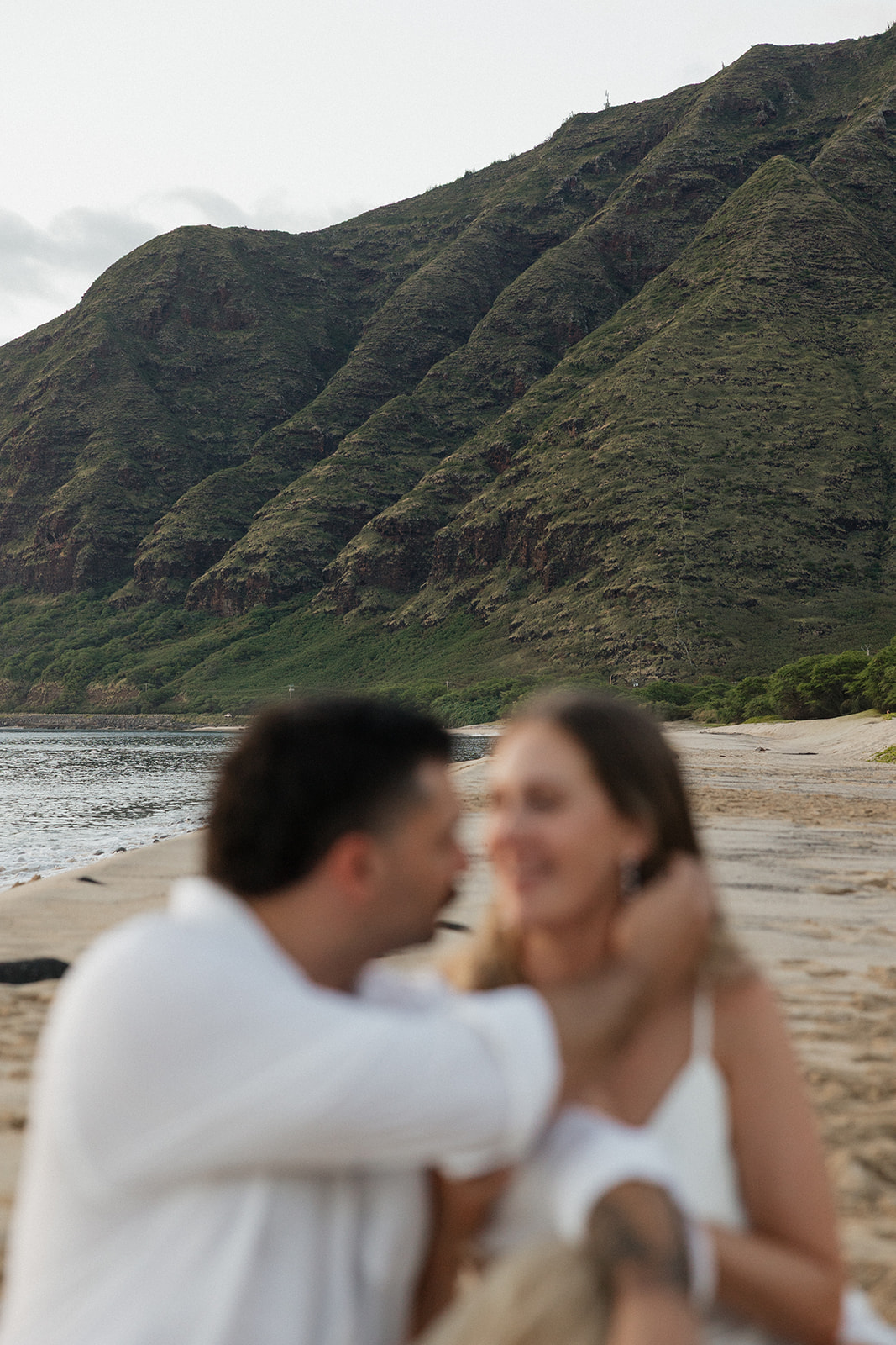 Soft, blurred close-up of the couple embracing on the beach as the groom holds his bride's face.