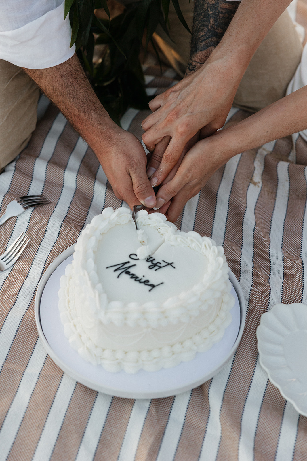 Close-up of the couple's hands cutting into their "Just Married" cake together.