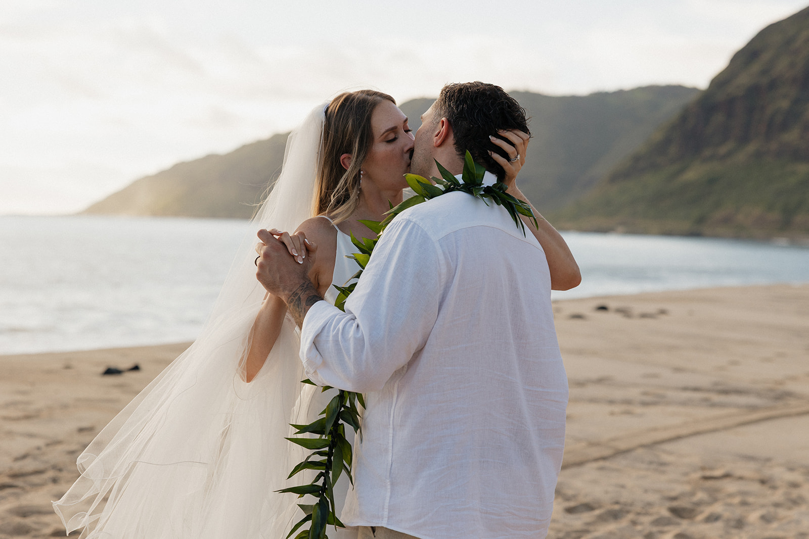 Bride and groom sharing a kiss on the beach as she runs her fingers through his hair during their first dance.