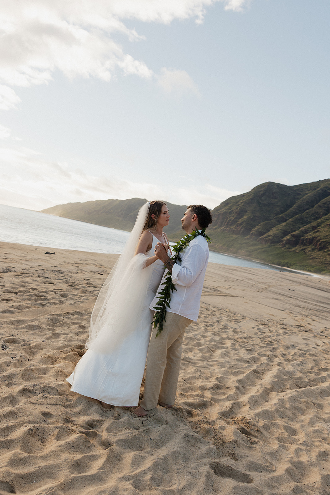 Bride and groom holding hands and gazing at each other on the sand.
