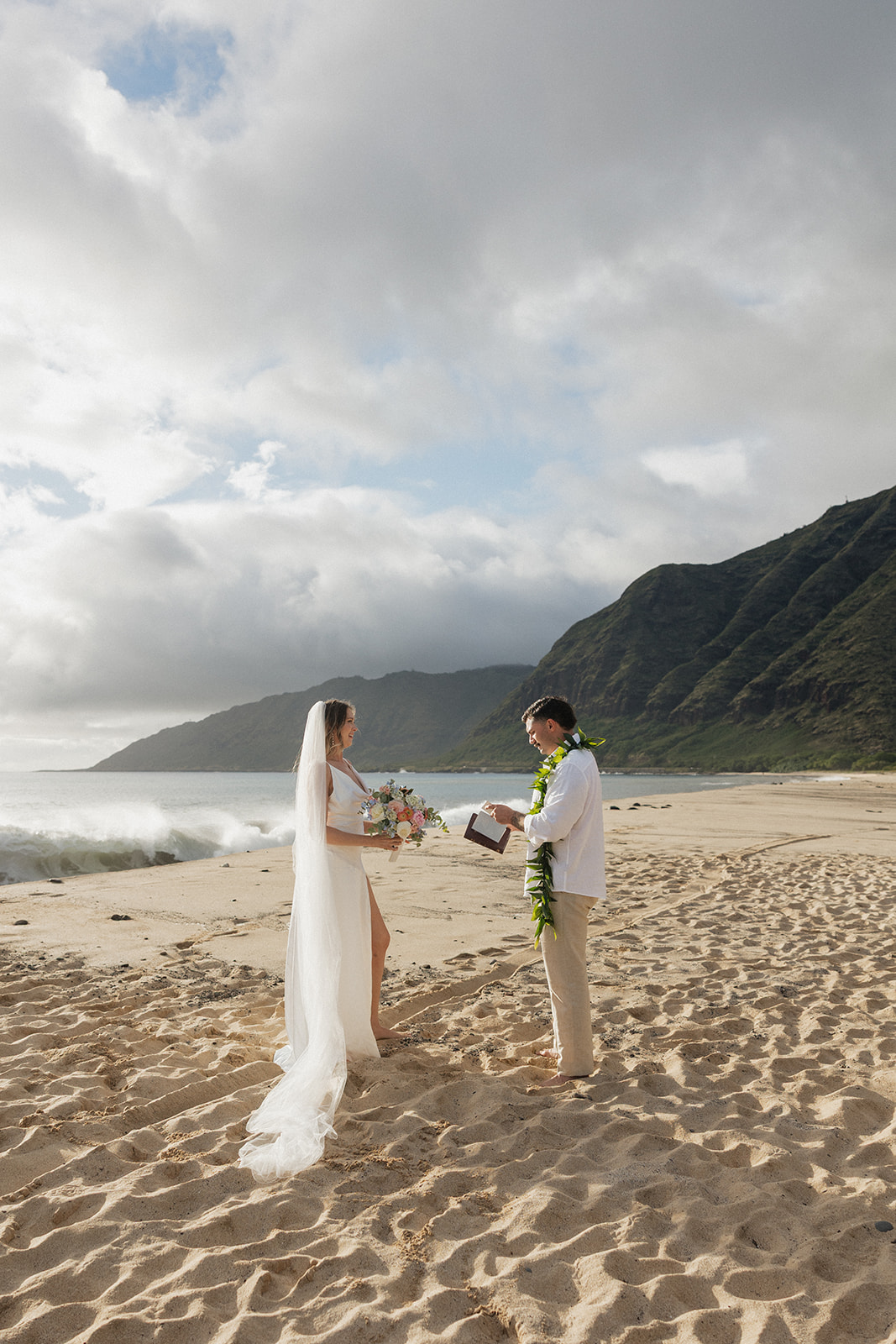 Bride and groom laughing together on the sand during their beach elopement vow ceremony.