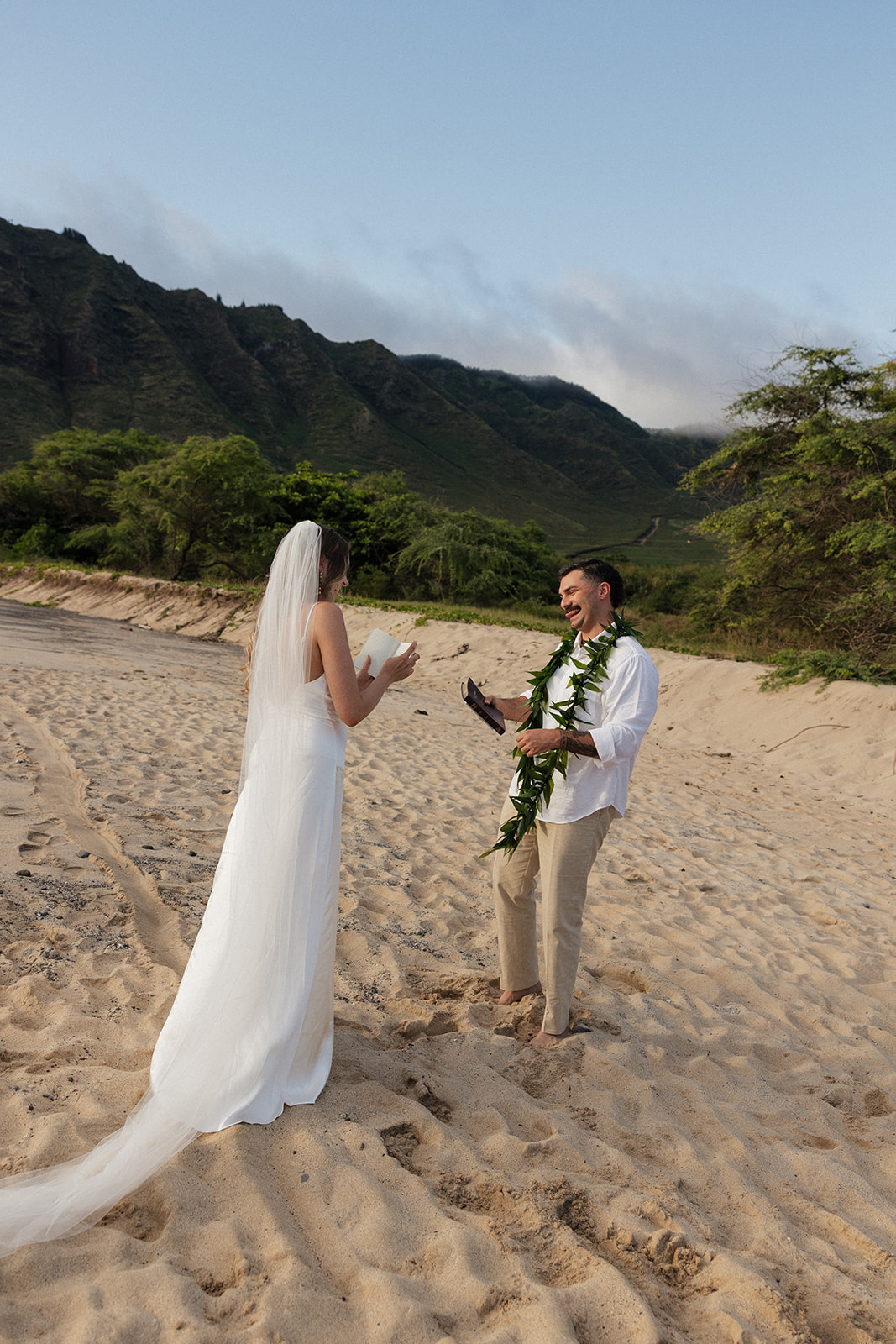 Groom laughing while the bride reads her vows during their intimate Oahu beach elopement.
