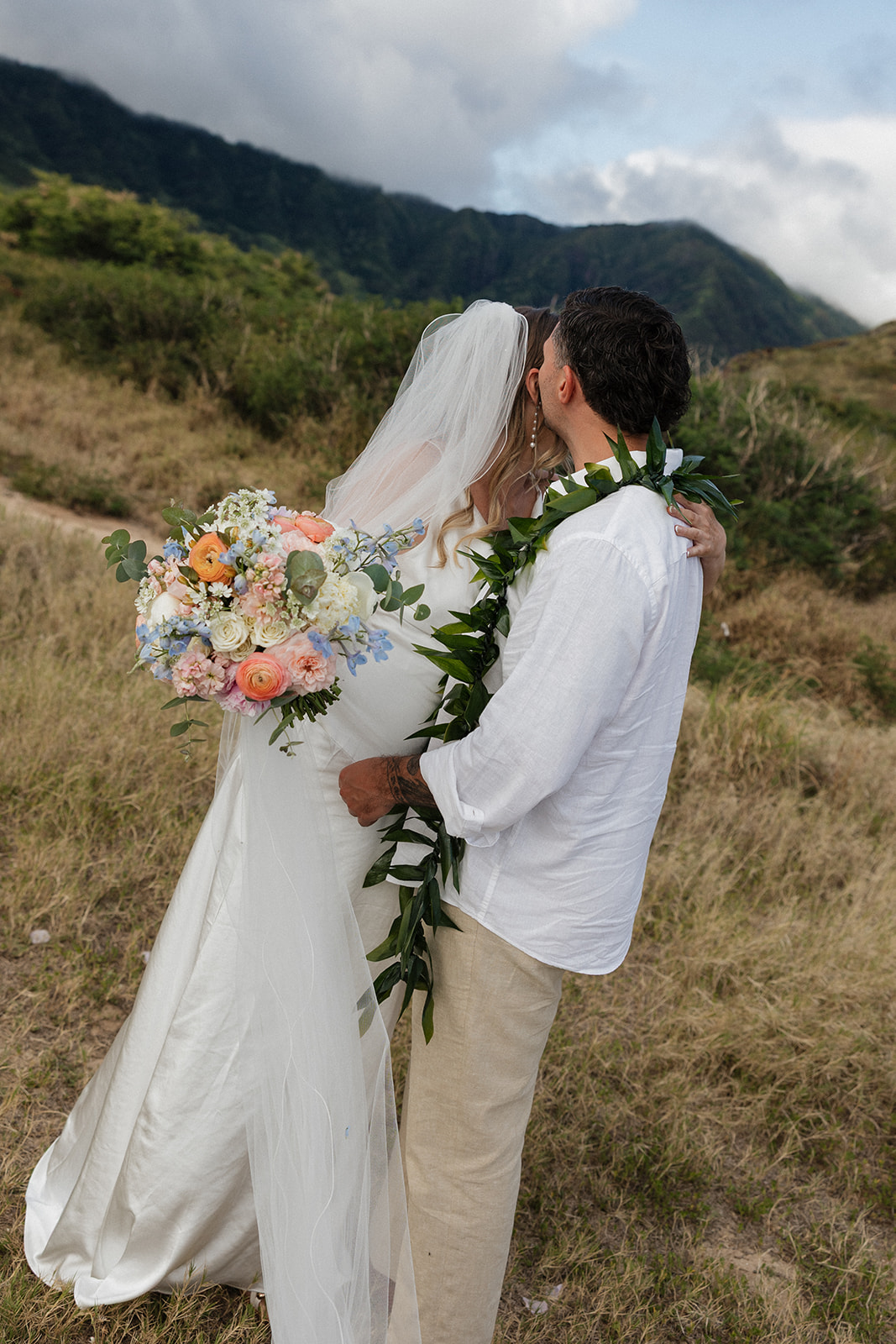 Bride and groom sharing an intimate kiss on a hillside overlooking the ocean during their beach elopement.