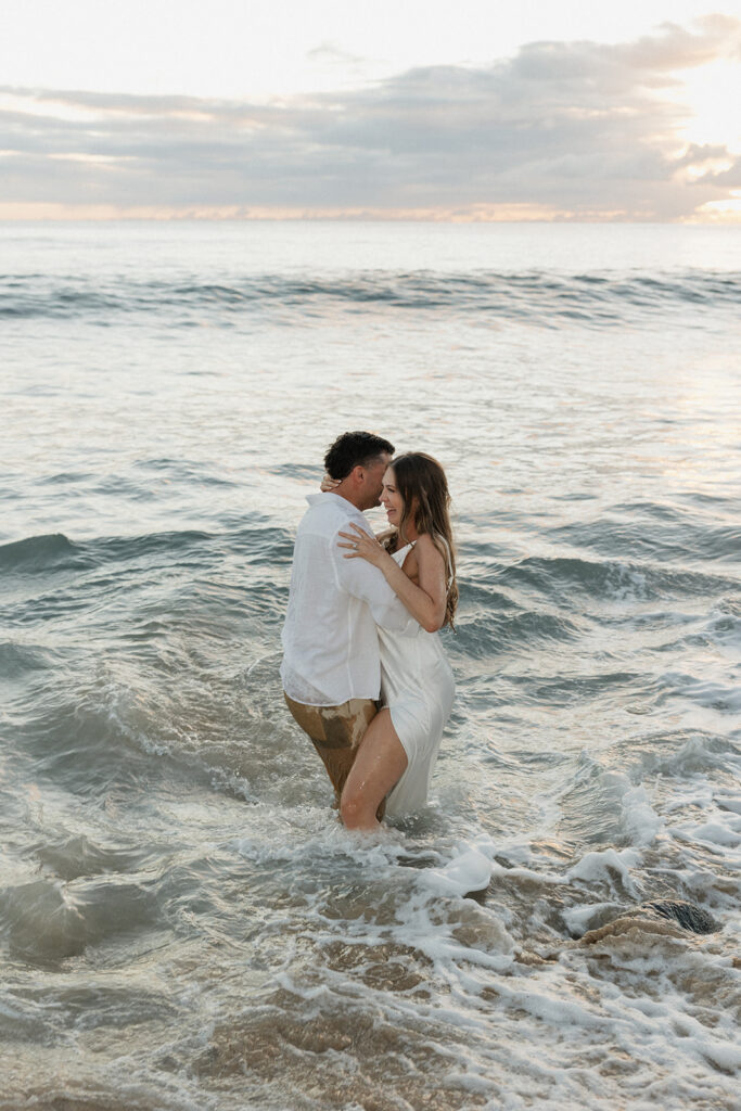 Couple holding each other in the ocean, foreheads together, completely soaked from their beach elopement.