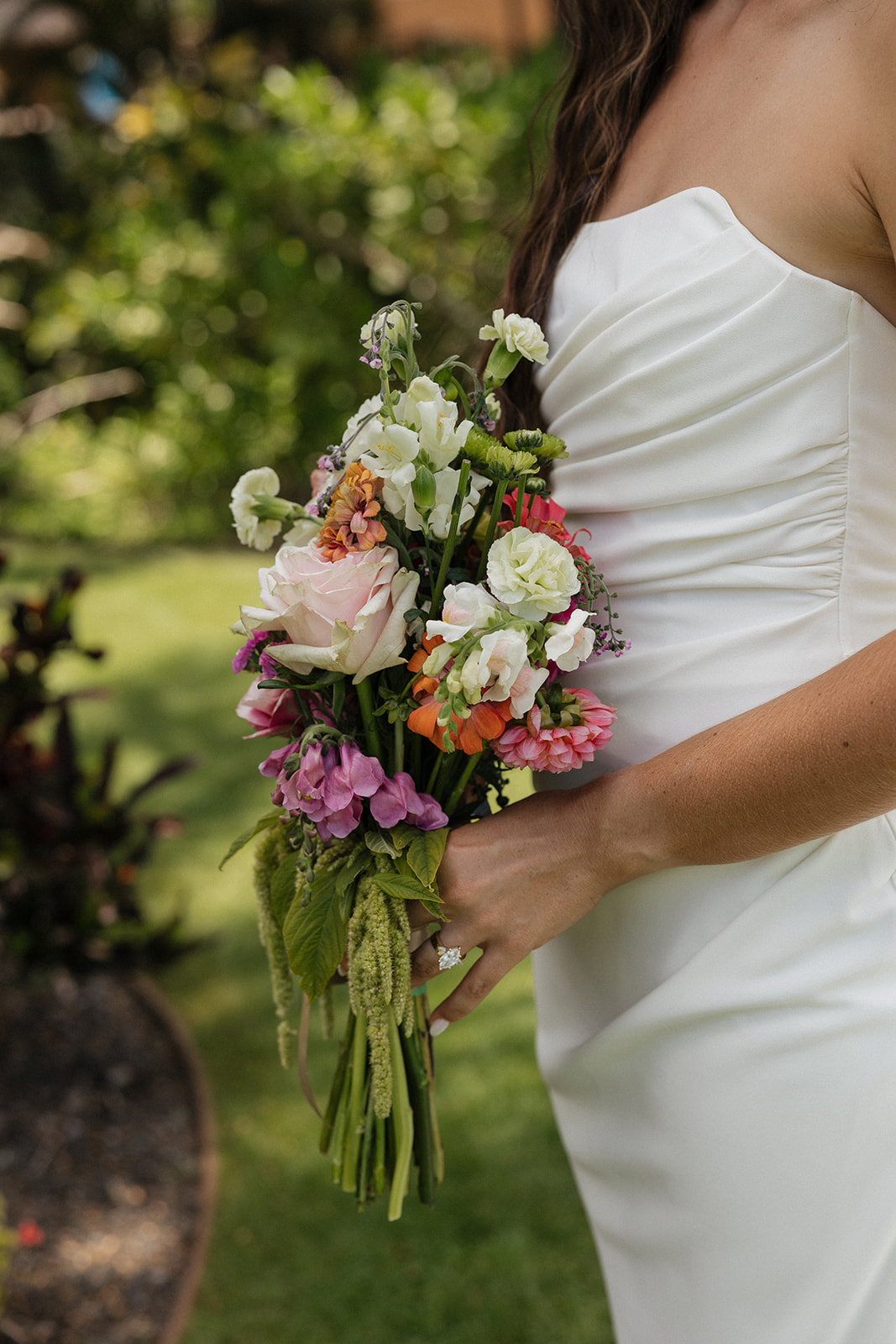Close up of the bride's bouquet featuring blush roses, dahlias and greenery against her ruched wedding gown at this Maui wedding venue.
