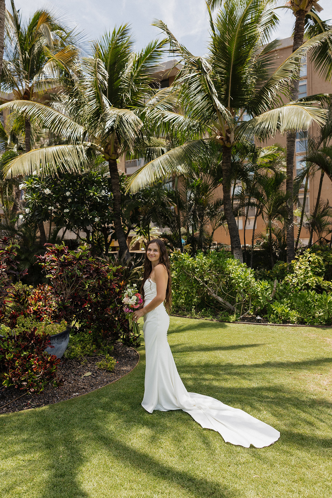 Bride glances back over her shoulder while walking through the garden, bouquet in hand.