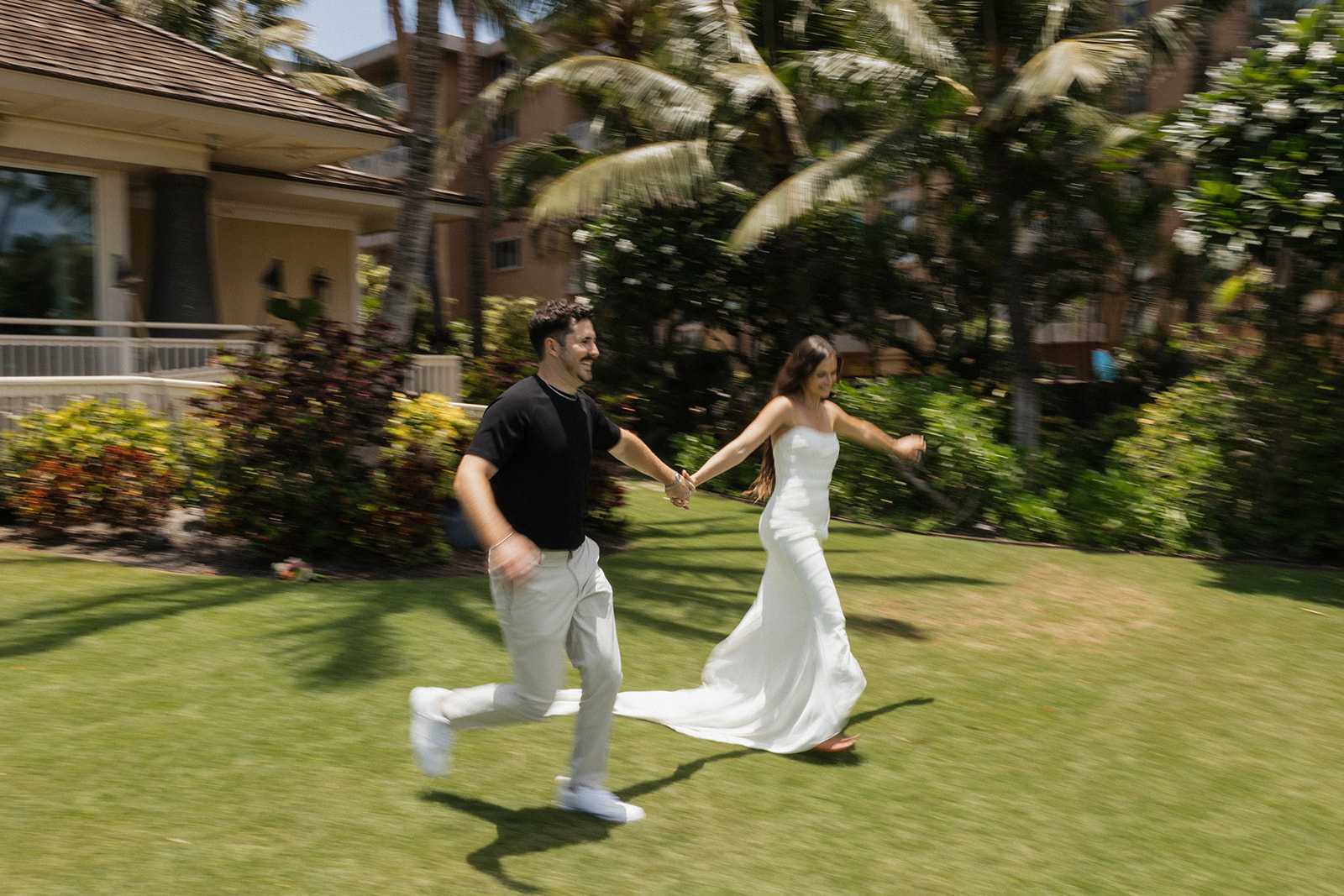 Bride and groom run hand in hand across the lawn, her train trailing behind them in motion.