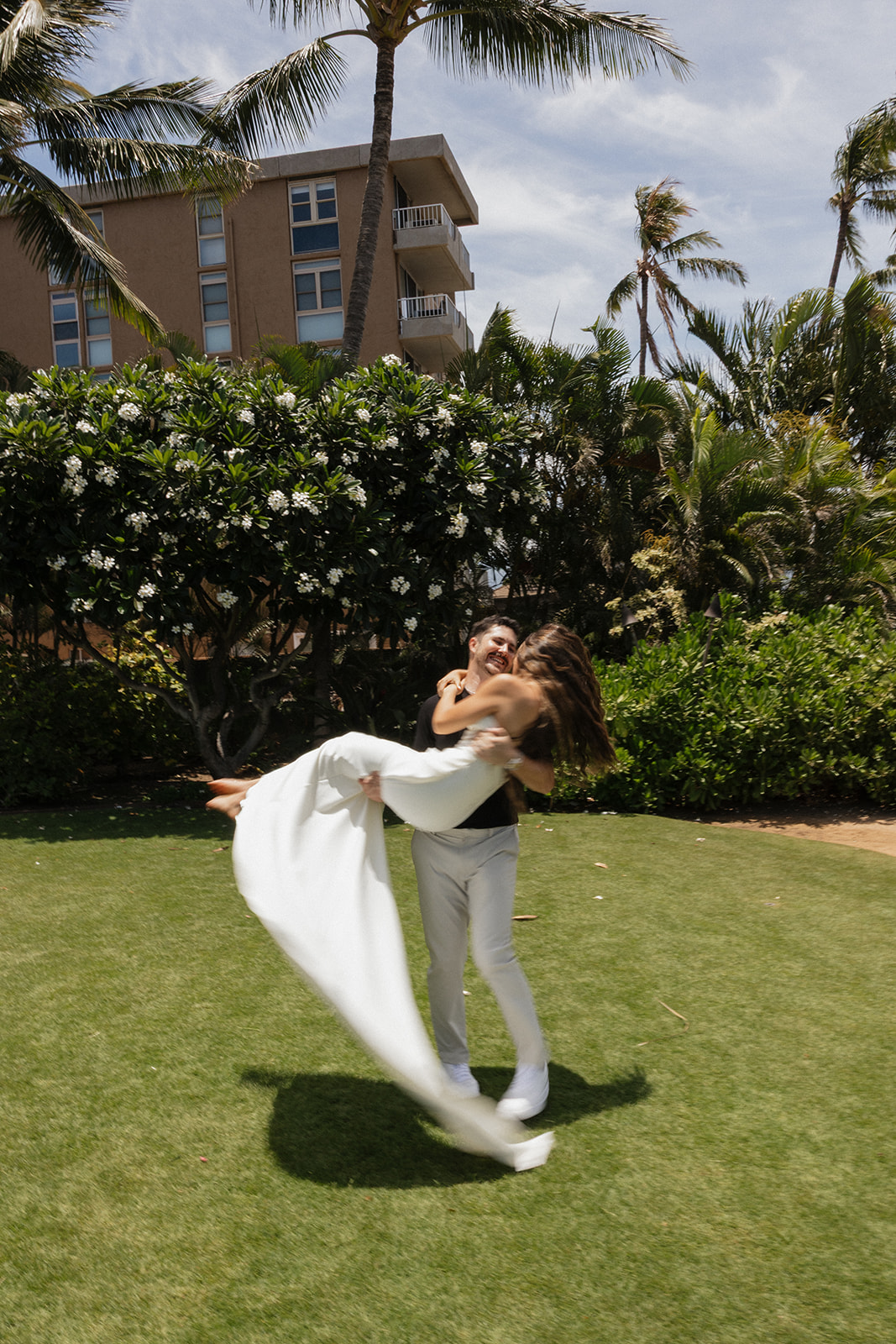 Groom lifts his laughing bride off the ground as her gown sweeps through the air at this Maui wedding venue.