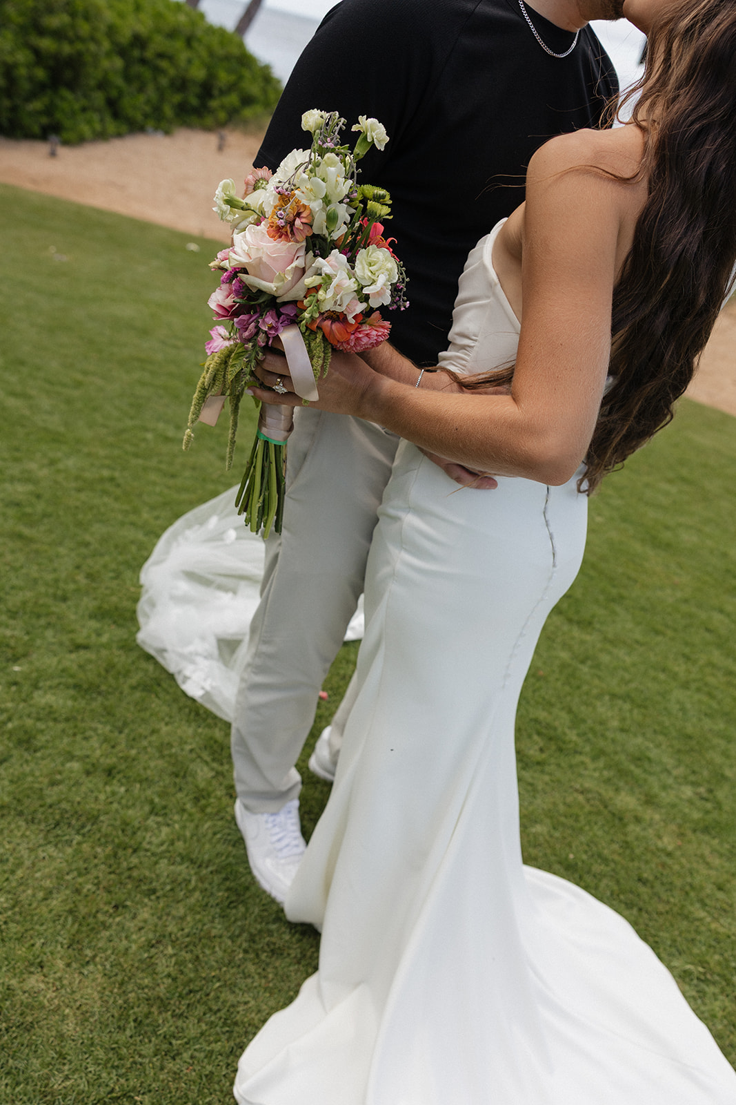 Close up of the bride's bouquet and wedding gown as the couple embraces on the grass.