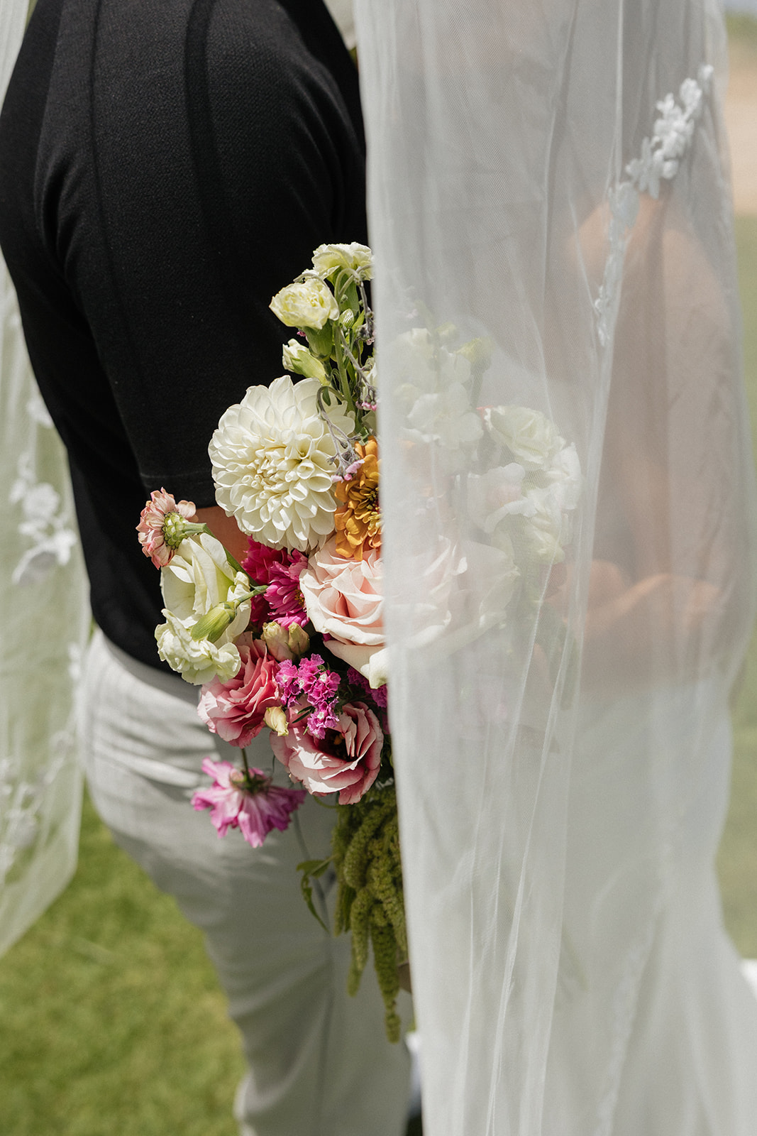 Bride's bouquet peeks out beside her veil and the groom's shoulder in this soft candid detail shot at this Maui wedding venue.