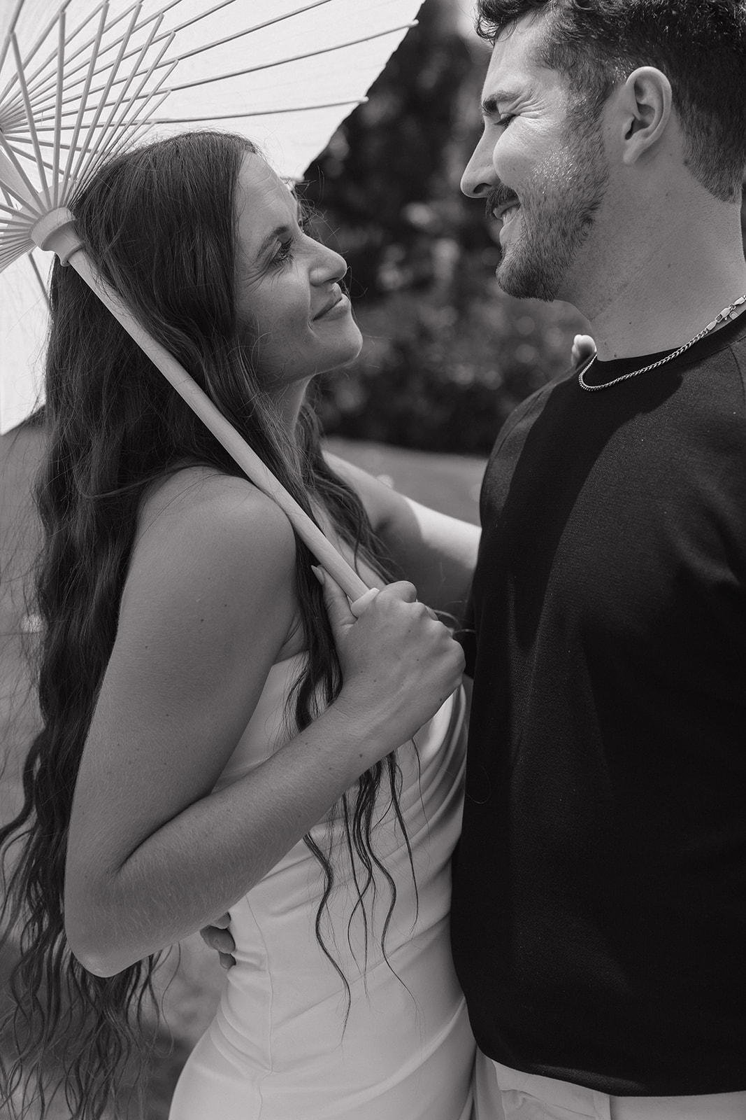 Black and white close up of the bride and groom smiling at each other under a parasol.