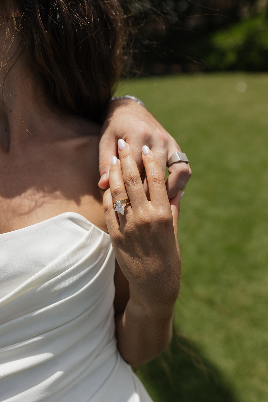 Close up of the bride's engagement ring resting on the groom's arm as they embrace.