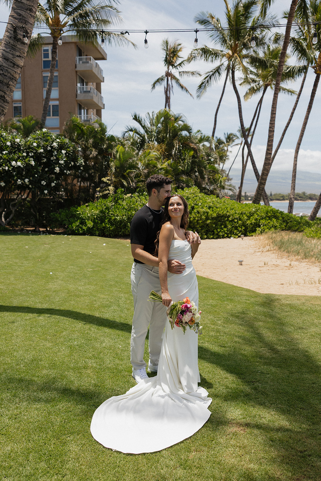 Groom embraces his bride from behind as they take in the ocean view together at this Maui wedding venue.