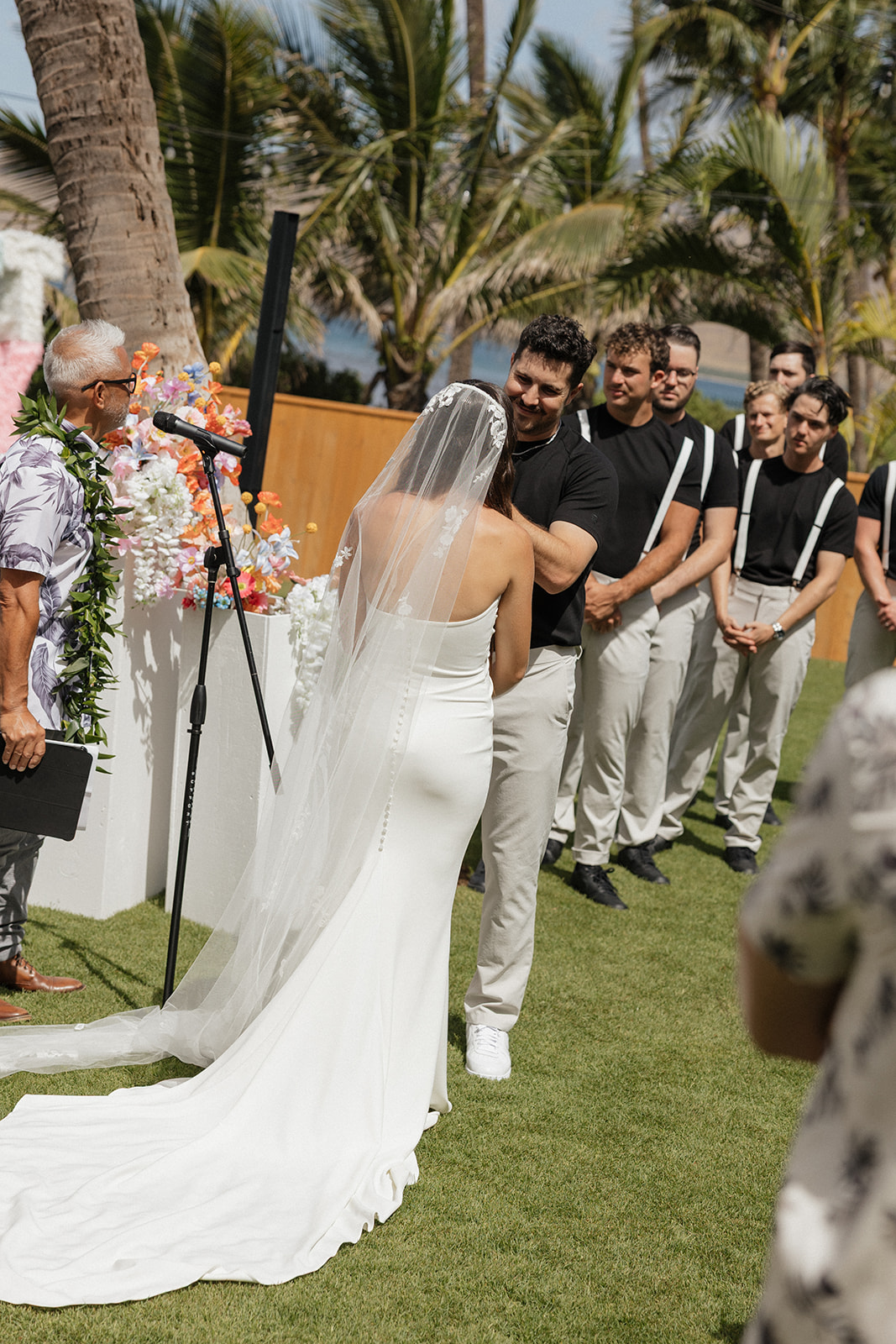 Bride and groom embrace in front of the groomsmen in matching black tees and suspenders during the ceremony.