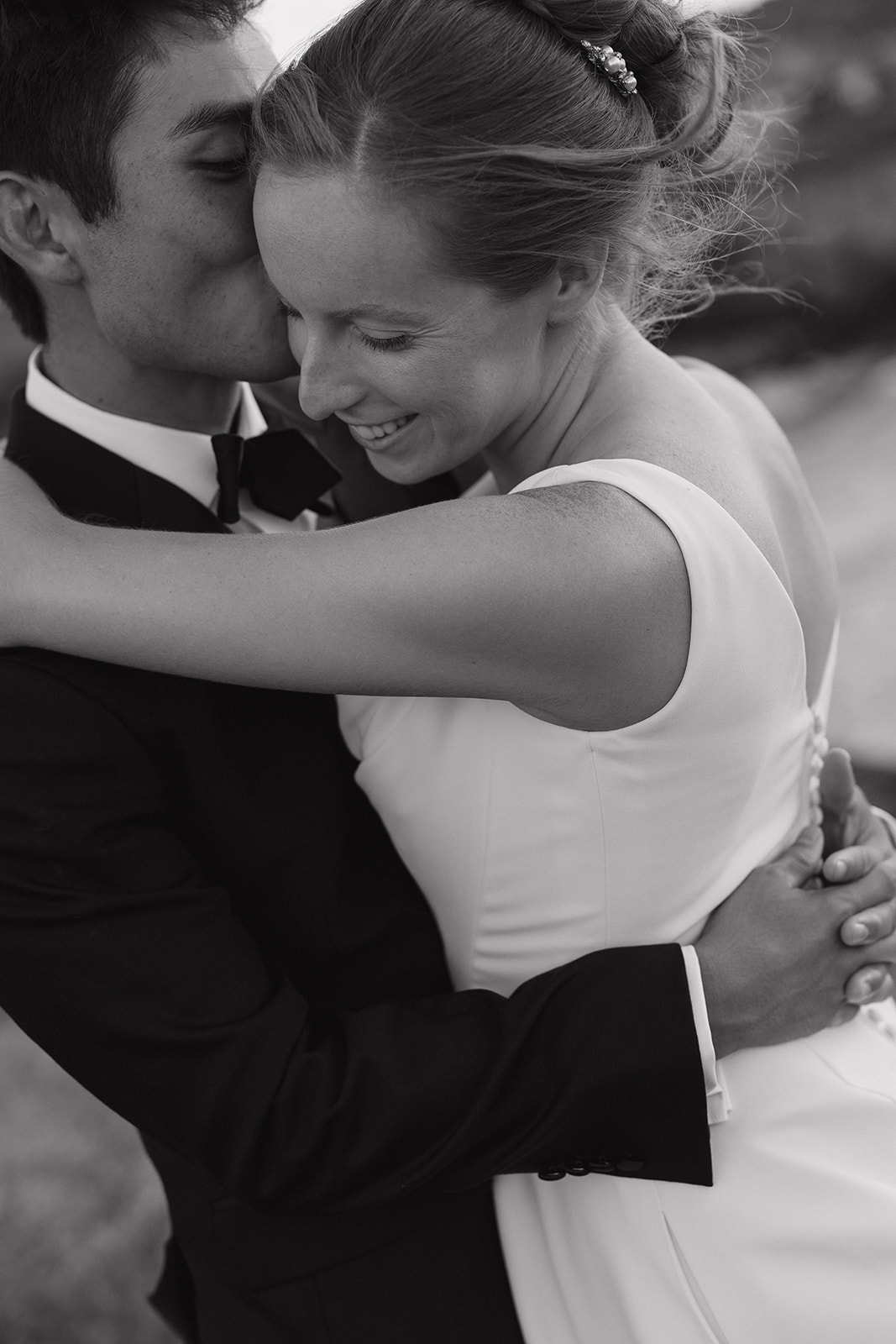 Black and white close up of a groom kissing his smiling bride's temple during their Maui Pineapple Chapel wedding portraits.