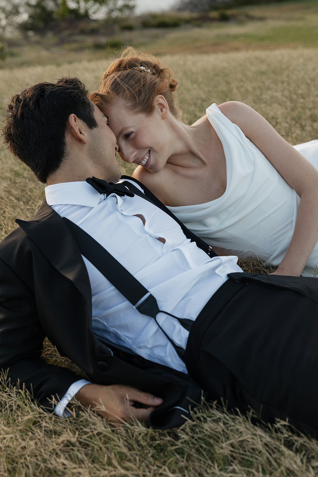 Bride and groom lying in the golden grass nose to nose and smiling during their Maui Pineapple Chapel wedding photos.