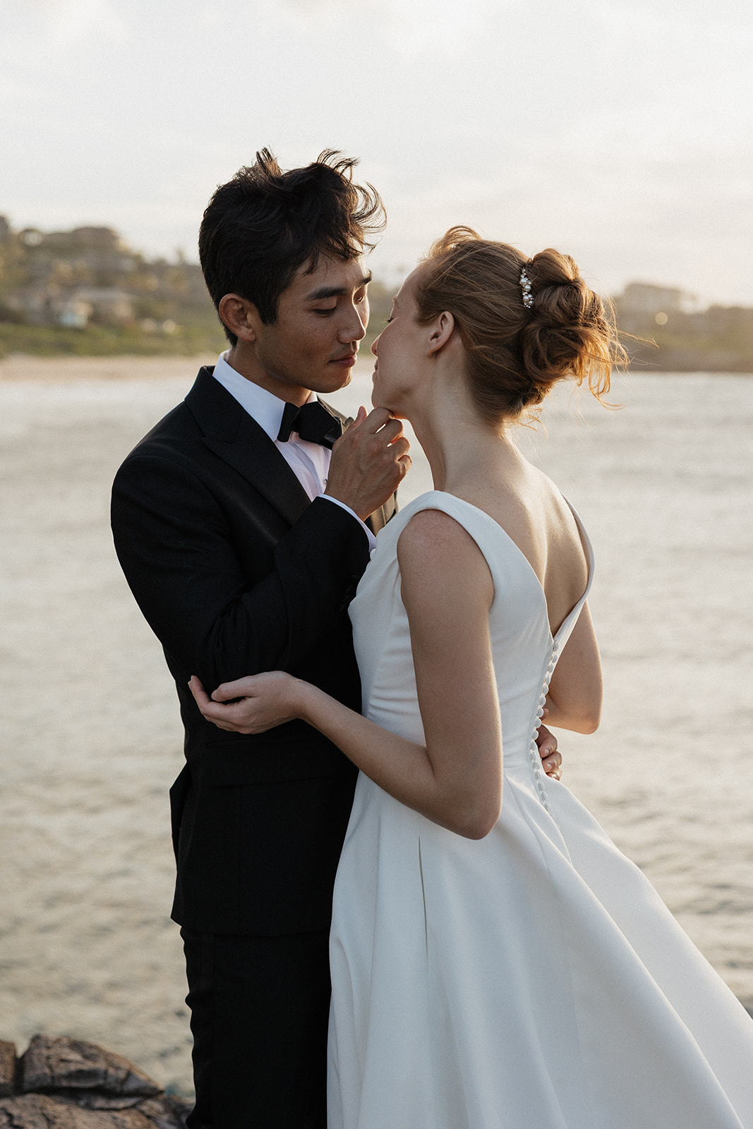 Groom gently touching his bride's chin for a romantic sunset portrait by the water at the Maui Pineapple Chapel.