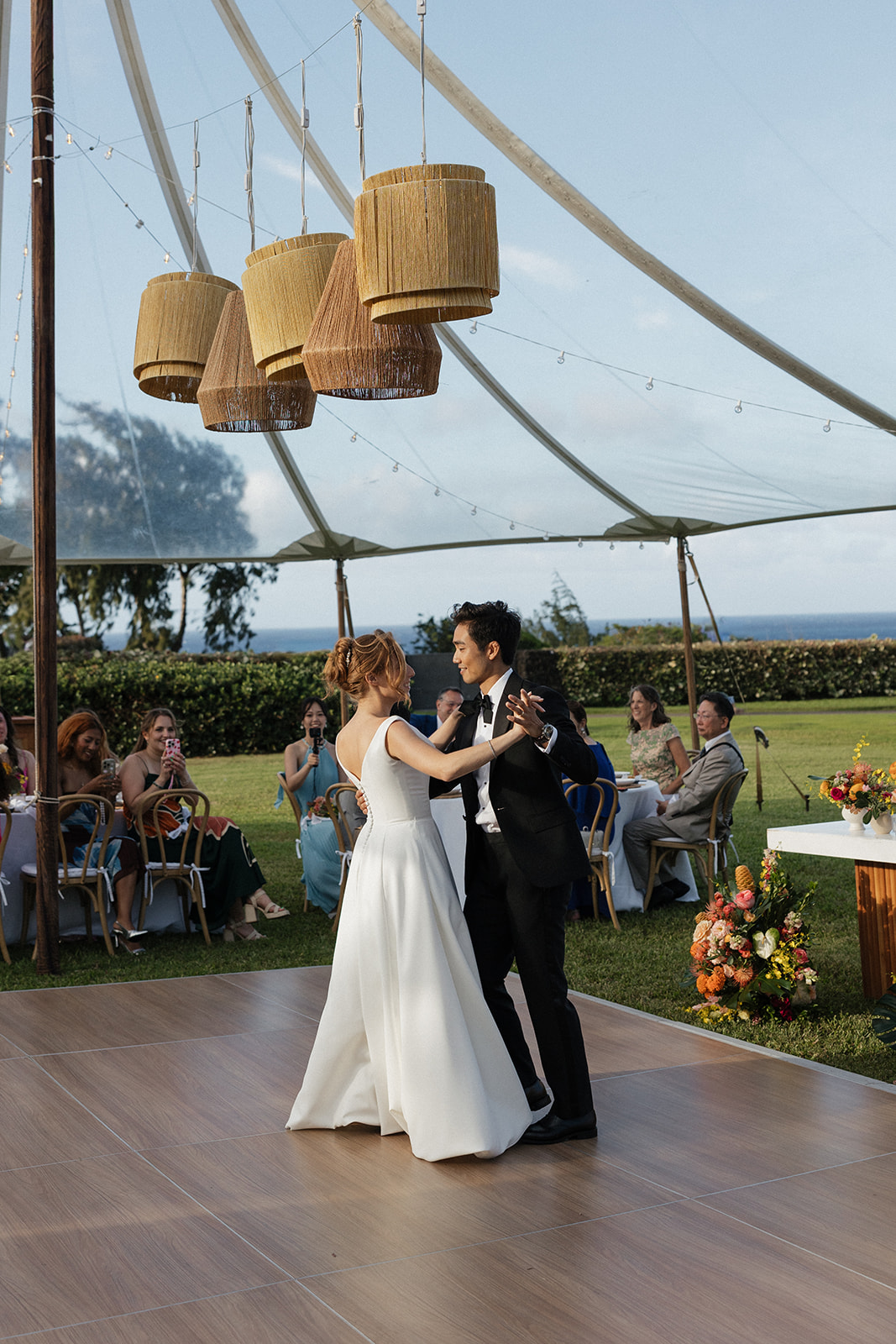 Bride and groom sharing their first dance under a clear tent with woven pendant lights at their Maui Pineapple Chapel wedding reception.