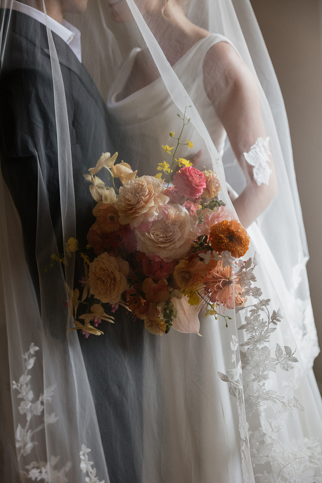 Close up of a tropical bouquet with orchids, garden roses, and ranunculus held beneath a lace trimmed veil at the Maui Pineapple Chapel.