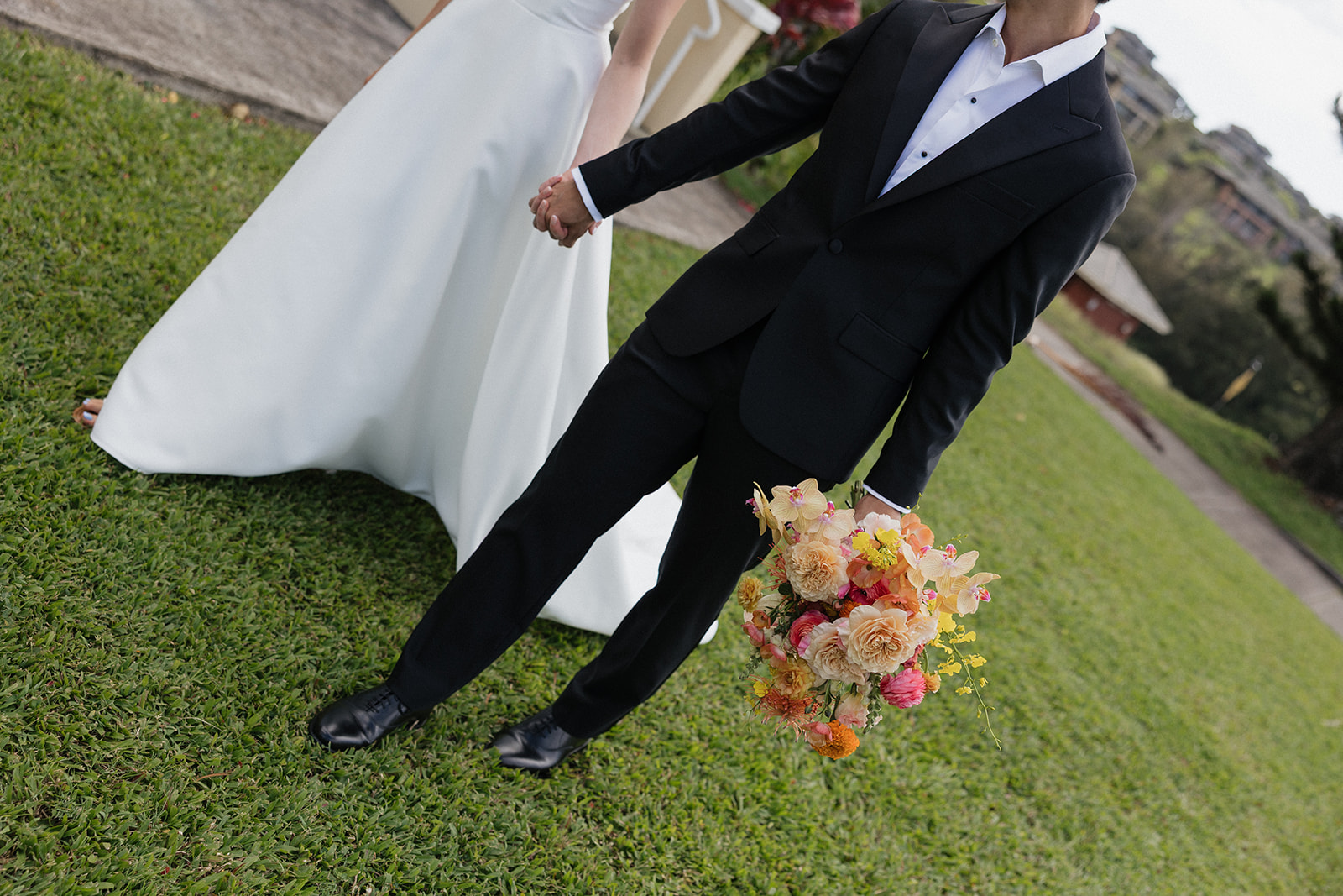 Bride and groom holding hands on the lawn while he carries a bright tropical bouquet at the Maui Pineapple Chapel.