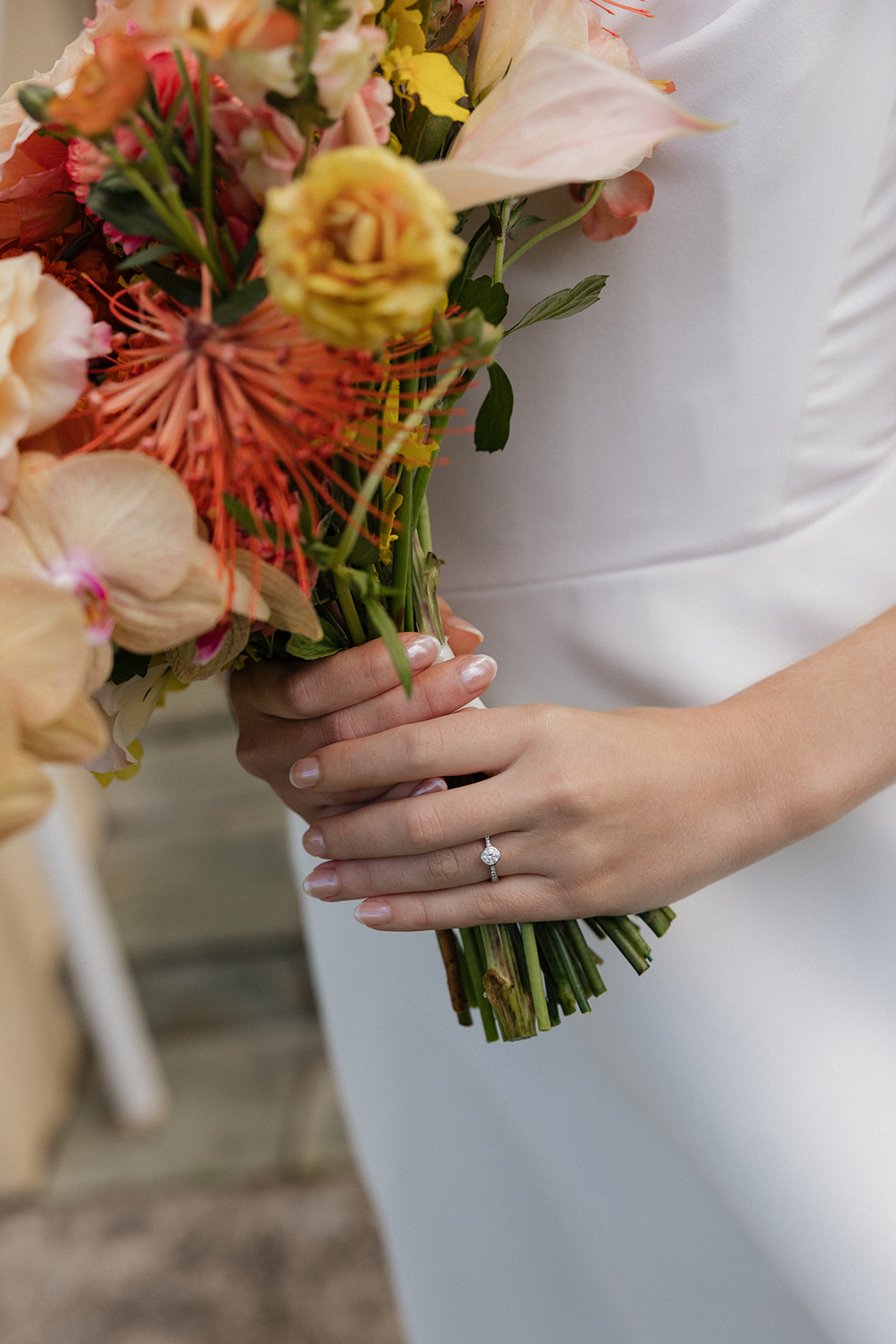 Close up of a bride's engagement ring on her hand as she holds a peach and orange tropical bouquet at the Maui Pineapple Chapel.