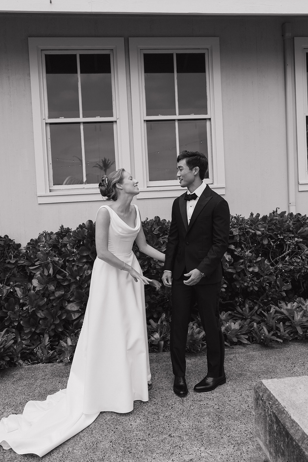 Black and white first look of a bride and groom laughing together outside the Maui Pineapple Chapel.