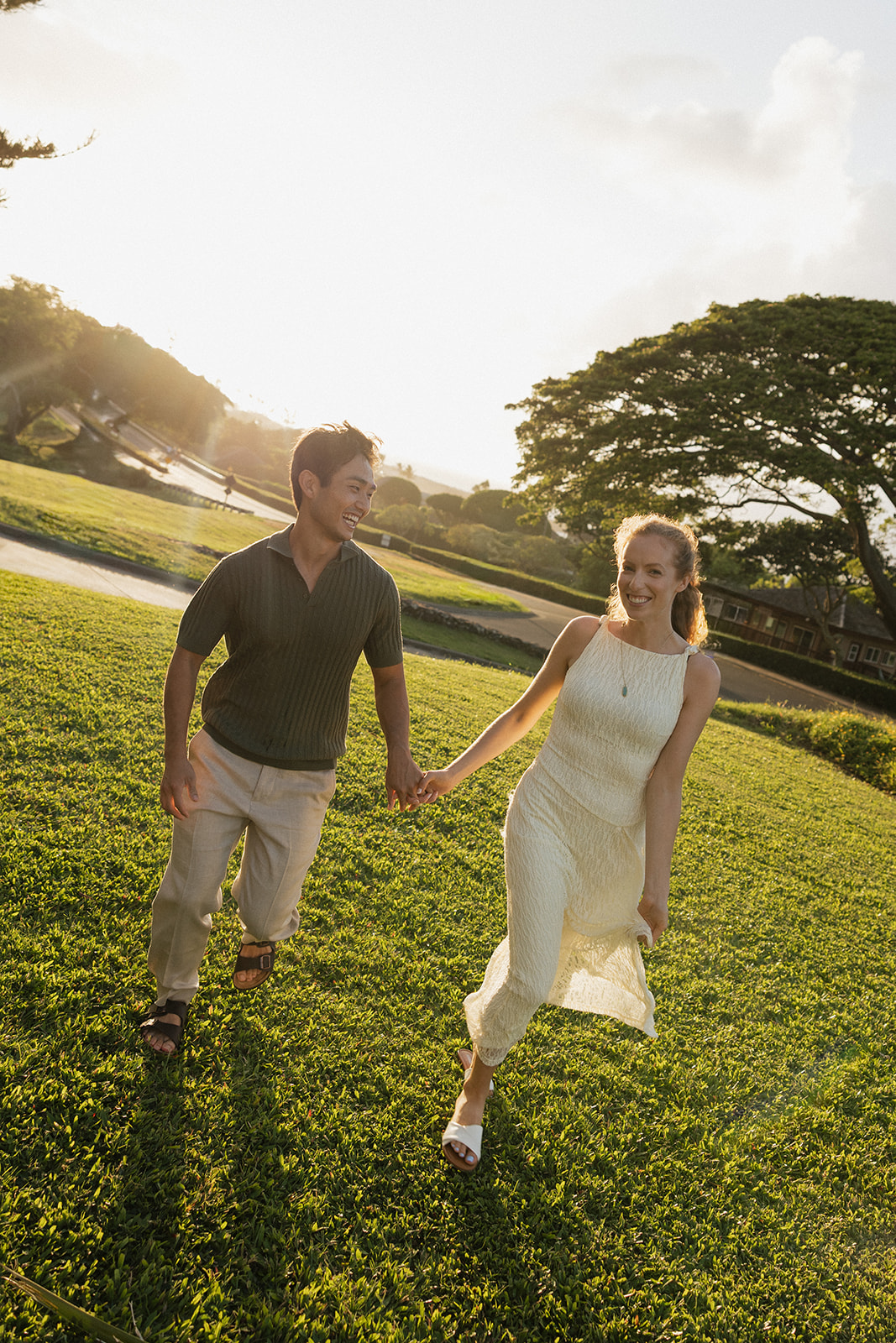 Couple laughing and holding hands as they walk across the green lawn at the Maui Pineapple Chapel in warm evening light.